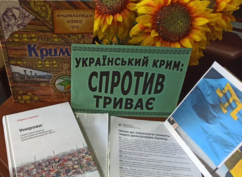 На столі - книги на тему: "Український Крим: спротив триває", за книгами - букет із соняхів.
