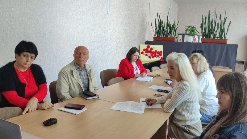 Група людей (чоловік і жінки) сидить за столом, їх погдяди зосереджені на екрані ноутбука.