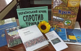 Книги на тему: "Український Крим: спротив триває" лежать/стоять на столі.  Між ними - квітка соняшника. 