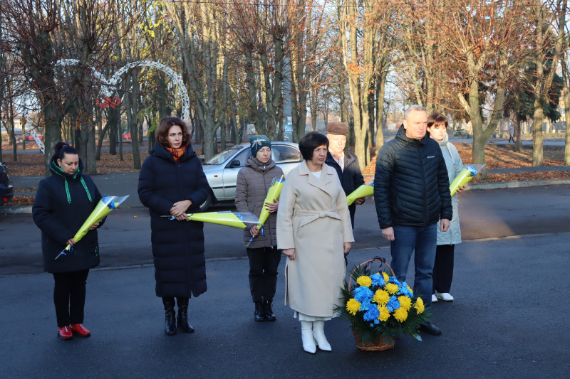 представники міської та районної влади стоять  з квітами  в руках, кошиком з жовтими і синіми квітами 