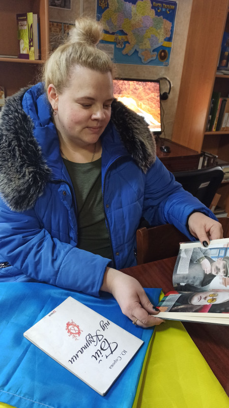 Відвідувачка бібліотеки тримає в руках книгу. Поряд на синьо-жовтому полотні лежить книга Ю.Сороки "Бій під Крутами"