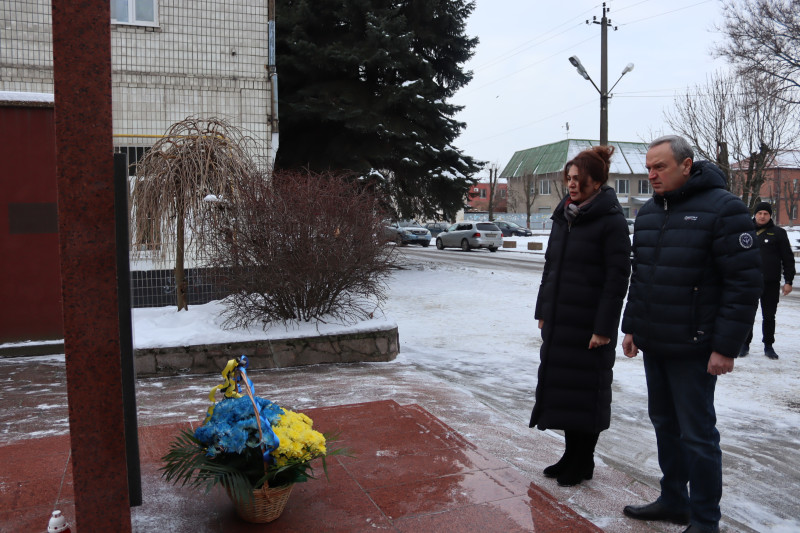 Міський голова Дмитро Зражевський та заступник голови Синельниківської районної військової адміністрації Тетяна Завалій вшановують пам'ять полеглих у війні хвилиною мовчання. У підніжжя пам'ятного знаку - кошик із синіми та жовтими квітами.