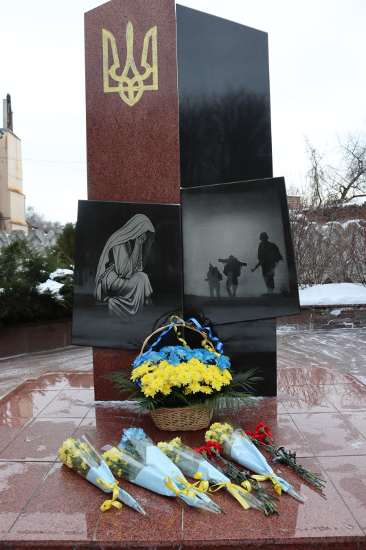 Пам'ятний знак на честь загиблих земляків -захисників і захисниць України: стела з двома плитами, угорі - Герб України. На одній  - мати, яка схилилася в скорботі. На іншій  - військові, які уходять вдалечінь. У підніжжя - кошик із синіми та жовтими квітами, букети квітів.