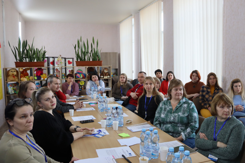 За довгим столом сидять учасники стратегічної сесії. На столі  - пляшки з водою, стаканчики, документи, чисті аркуші.   