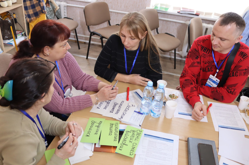 Триває обговорення серед учасників заходу, які сидять за столом: три дівчини та молодий чоловік. На столі - картки білого та  салатного кольору з написами, маркери, вода в пляшках. 