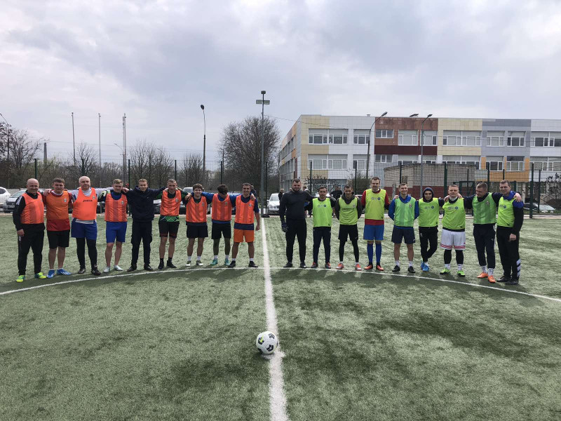Футболісти стоять на полі півколом. Перед ними - м'яч. На задньому фоні - частина будівлі.