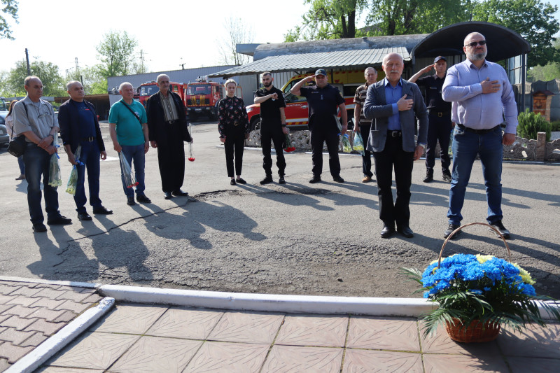 Учасники заходу: ліквідатори аварії на ЧАЕС, правовохоронці, представники міської  та районної влади стоять. Перші - тримають у руках квіти, другі - праву руку біля серця, треті  - віддаючи честь.  Перед ними - кошик із квітами.