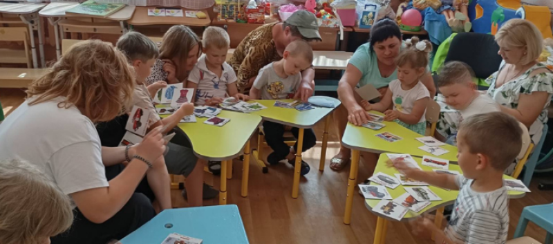 Діти разом із вихователями, матусями сидять за столиками і розглядають картинки.