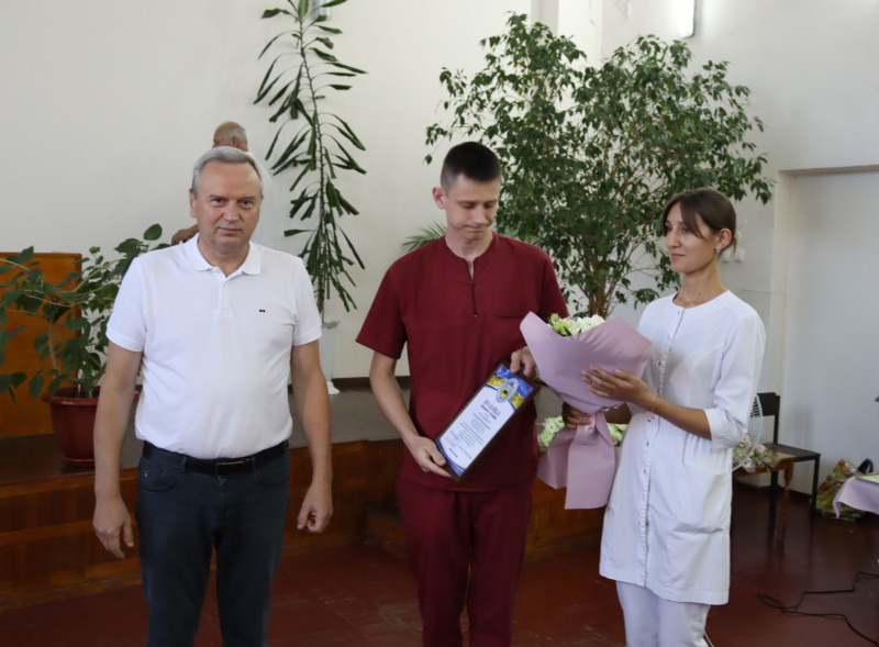 Міський голова Дмитро Зражевський стоїть разом із молодими медичними працівниками. У чоловіка в руках - відзнака міського голови, у дівчини - квіти.