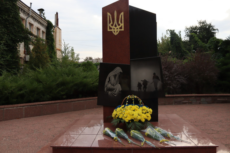 Пам'ятний знак на честь загиблих Захисників і Захисниць України. У підніжжя  - кошик із синьо-жовтими квітами, букети квітів.