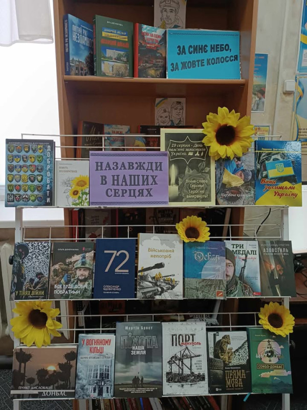 Полиця з книгами на тему: "Назавжди в наших серцях", прикрашена квітами соняхів.