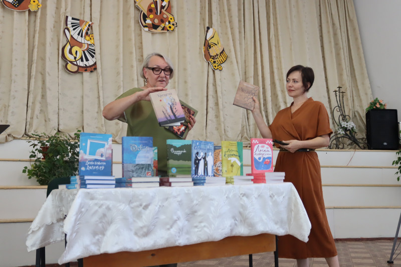 Письменниця Людмила Охріменко стоїть за столом з книгою  в руках. На столі - її авторські книги. Поряд стоїть жінка, тримає в руці теж книгу. 