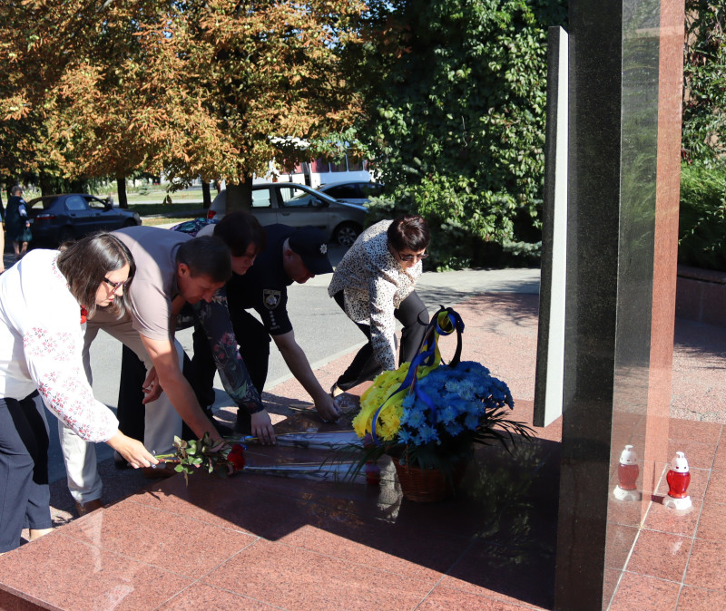 Чоловіки та жінки покладають квіти до пам'ятного знаку загиблим воїнам.