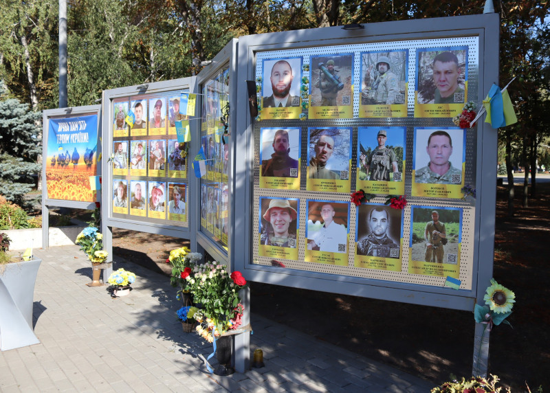 Пам'ятна дошка з фотографіями полеглих земляків, прикрашена квітами, прапорцями.