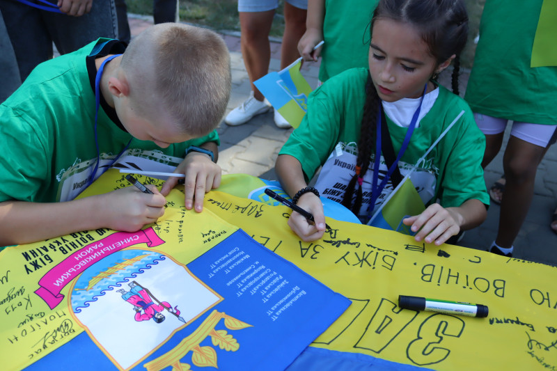 Хлопець та дівчинка ставлять свої підписи на прапорі.
