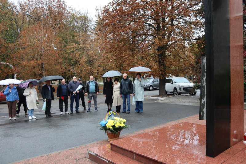 Міський голова Дмитро Зражевський, начальник Синельниківської районної військової адміністрації Світлана Назарчук, інші представники міської та районнної влади, громадськості стоять у хвилині мовчання перед  пам'ятним знаком полеглим за Україну воїнам. Перед знаком  - кошик із квітами.