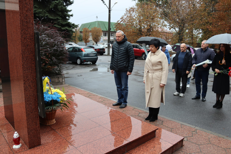 Міський голова Дмитро Зражевський, начальник Синельниківської районної військової адміністрації Світлана Назарчук, інші представники міської та районнної влади, громадськості стоять у хвилині мовчання перед  пам'ятним знаком полеглим за Україну воїнам.  У підніжжя  - кошик із квітами.