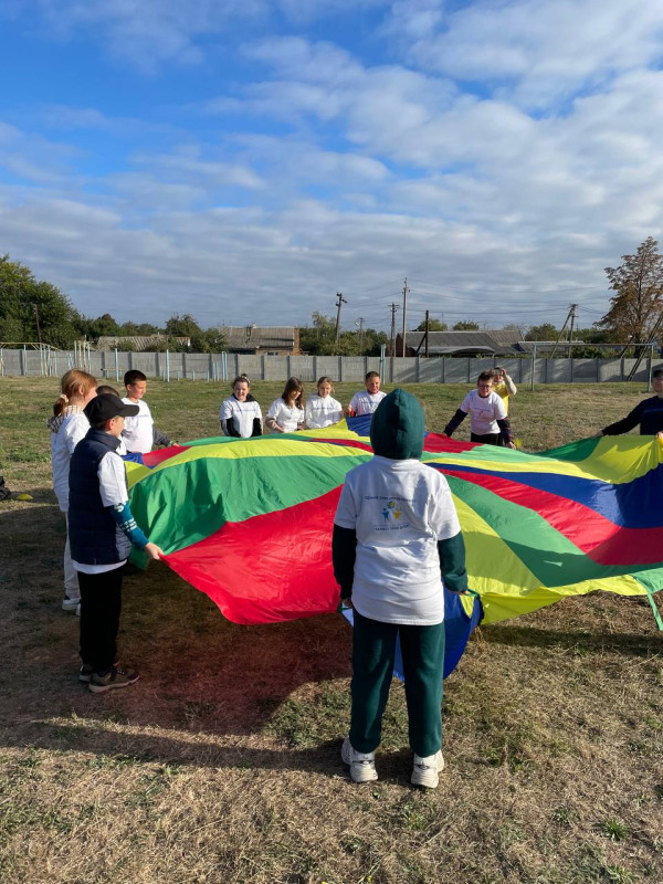 Діти стоять на траві, тримають руками коло із тканини з різнокольорових трикутничків. 
