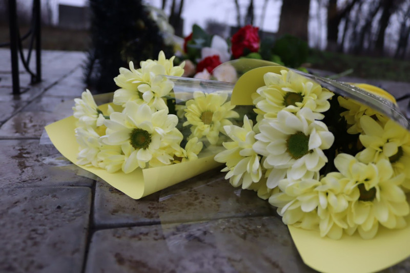 Жовті хризантеми лежать на плитці біля пам'ятного знака жертвам голодомору.