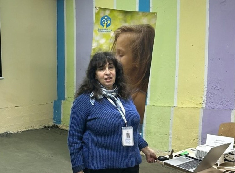 Жінка виступає з промовою. На столі  - відкритий ноутбук.