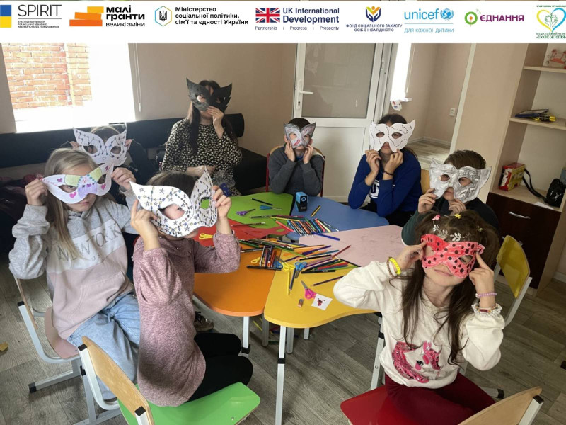 Діти сидять за столом разом із наставницею. На обличчях - маски, зроблені власноруч.
