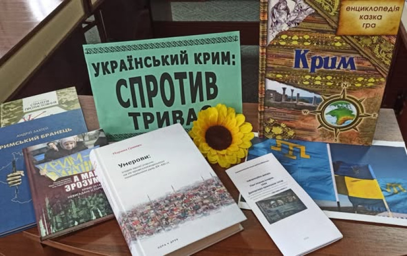 Книги на тему: "Український Крим: спротив триває" лежать/стоять на столі.  Між ними - квітка соняшника. 