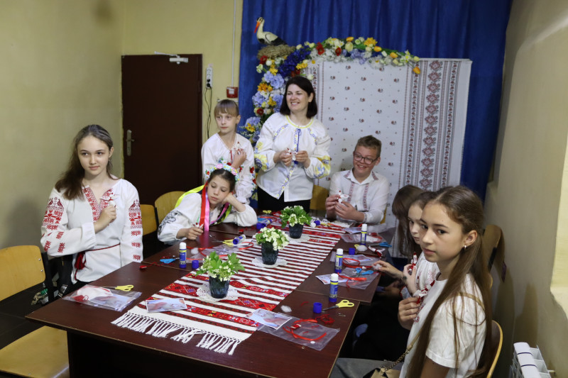 Діти разом із керівником за столом. На столі лежать роботи, нитки. Усі дивляться вперед. 