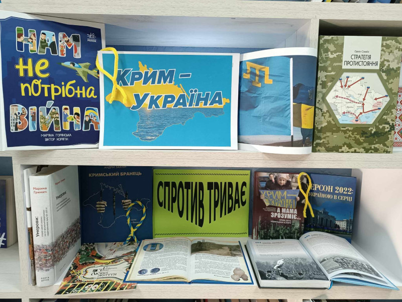 Виставка українських книжок, матеріалів на тему супротиву та війни, розміщена на книжковій полиці. На виставці видно написи &laquo;Нам не потрібна війна&raquo;, &laquo;Крим - Україна&raquo; та &laquo;Спротив триває&raquo;.