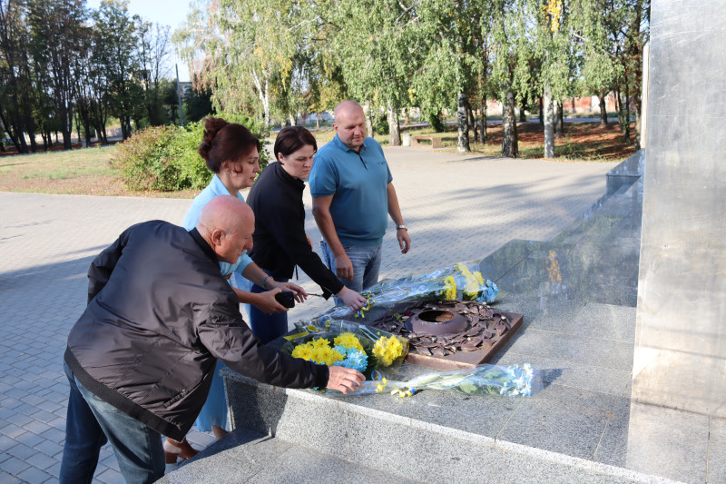 Група людей покладає синьо-жовті квіти до меморіалу у парку.